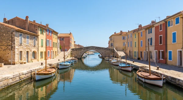 Photographie réelle en plein jour d'un élément urbain ou architectural caractéristique de Martigues, illustrant l'identité visuelle provençale de la commune. L'image pourrait montrer les canaux typiques de Martigues avec bâtiments colorés en arrière-plan, une vue du vieux port avec bateaux de pêche traditionnels, une rue pavée du centre historique avec architecture provençale, ou l'église Sainte-Madeleine reflétée dans les eaux. La photographie doit être de qualité professionnelle, prise en conditions d'éclairage naturel jour, sans texte ni logo, permettant une identification claire de Martigues comme localité de Provence-Côte d'Azur.